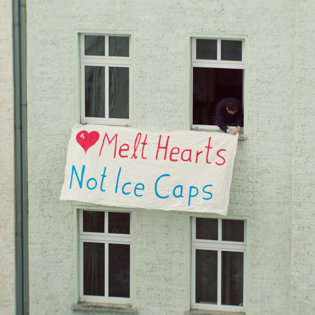 A banner reading 'Melt Hearts Not Ice Caps' hung from an apartment window